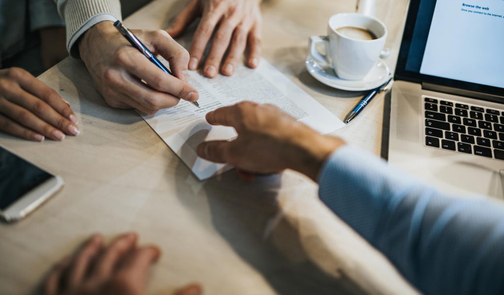 Unrecognizable man signing a contract while financial advisor is aiming at the place he need to sign.