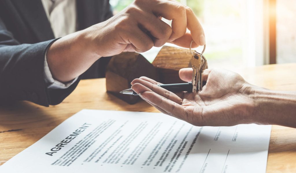 Estate agent giving house keys to customer and sign agreement in office.
