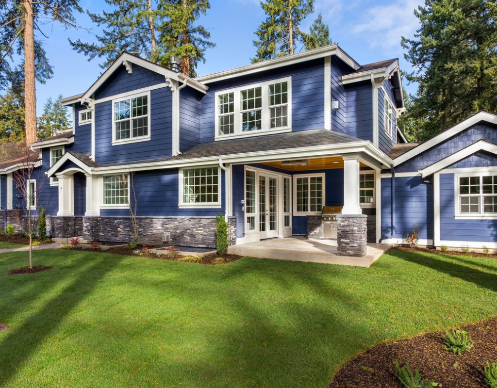 facade of home with manicured lawn, and backdrop of trees and blue sky